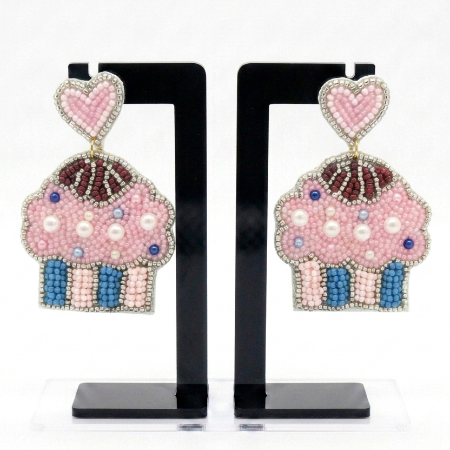 A pair of cupcake-shaped beaded earrings displayed on black standees against a white background. The earrings feature a pink heart-shaped top with a gold connector, a pink cupcake body with blue and white beading, and small blue and white pearl-like accents.